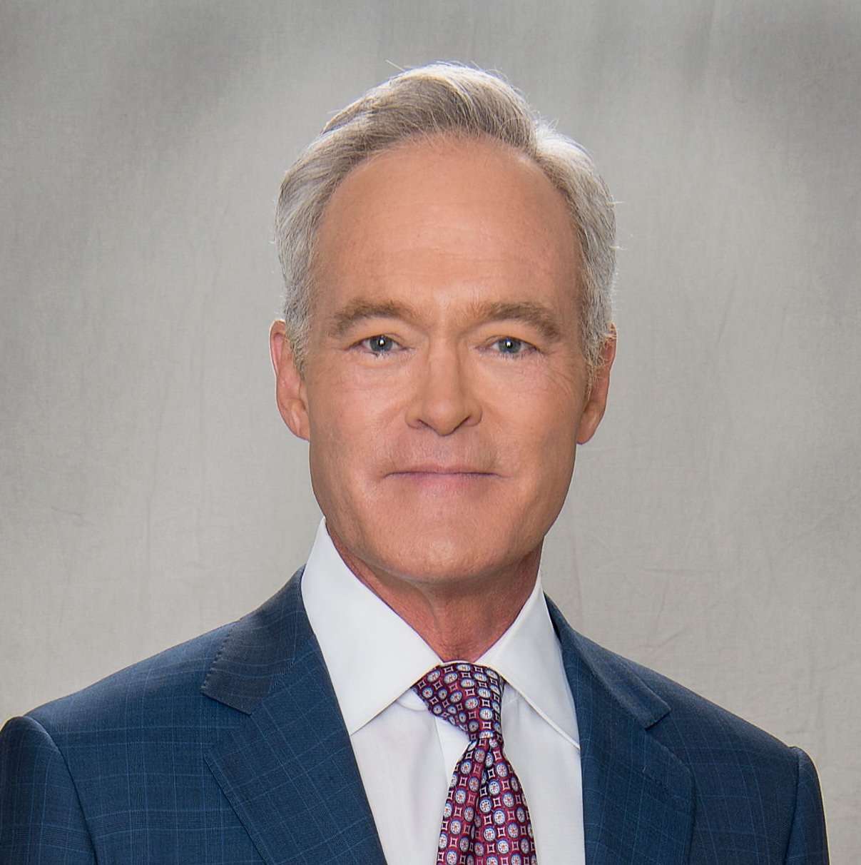 male with gray hair wearing white shirt, dark blue blazer and red and white tie.